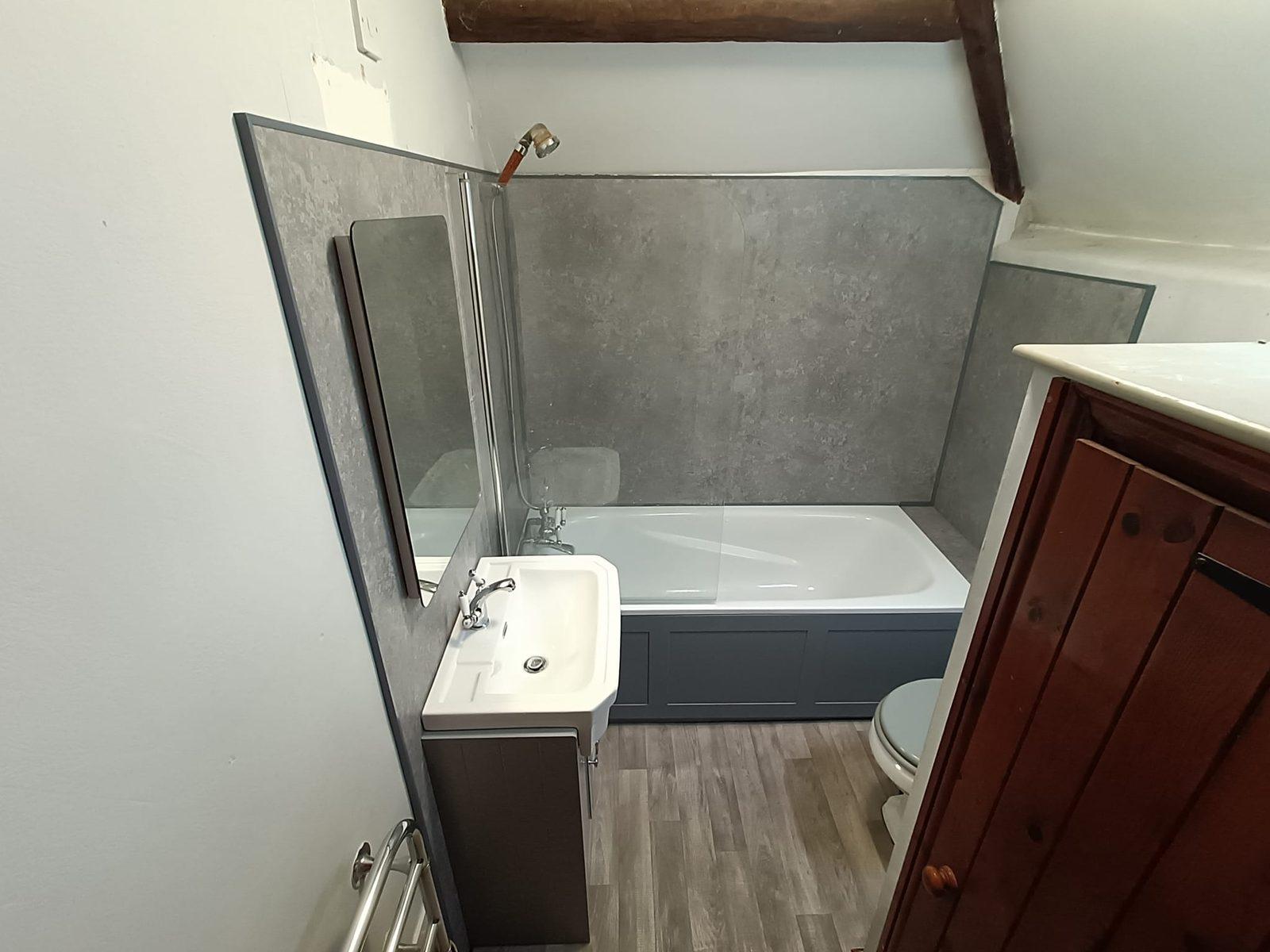 Renovated bathroom with grey panelling and a navy bath