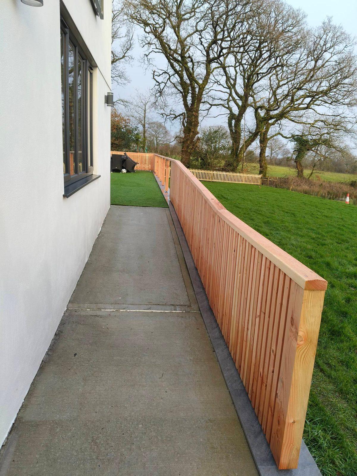 New timber slatted fence and concrete path beside a rendered house