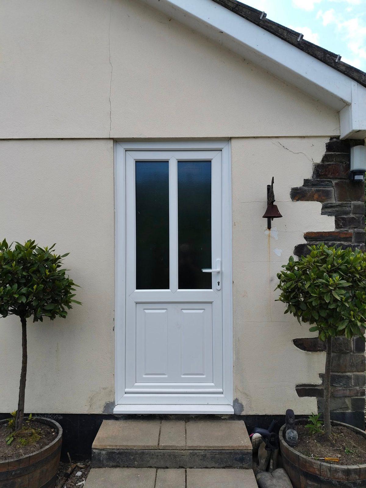 New white uPVC door in a rendered wall flanked by bay trees