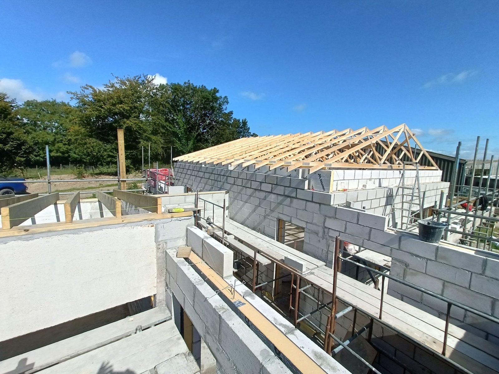 New build house with blockwork walls and timber roof trusses against blue sky