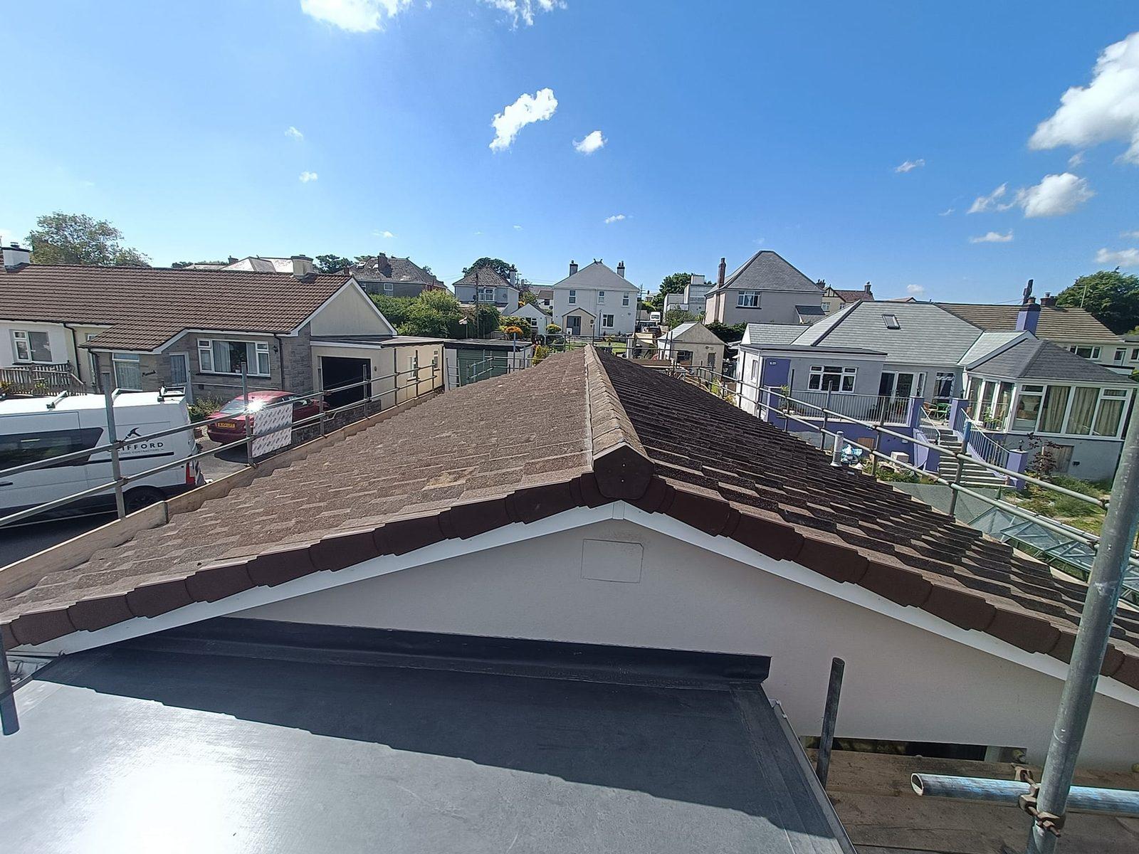 Newly tiled pitched roof with flat-roof section against blue sky